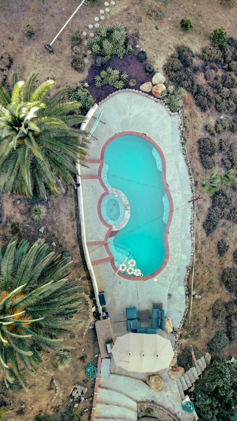 A construction crew shaping a backyard swimming pool shell with rebar and machinery under sunny skies.
