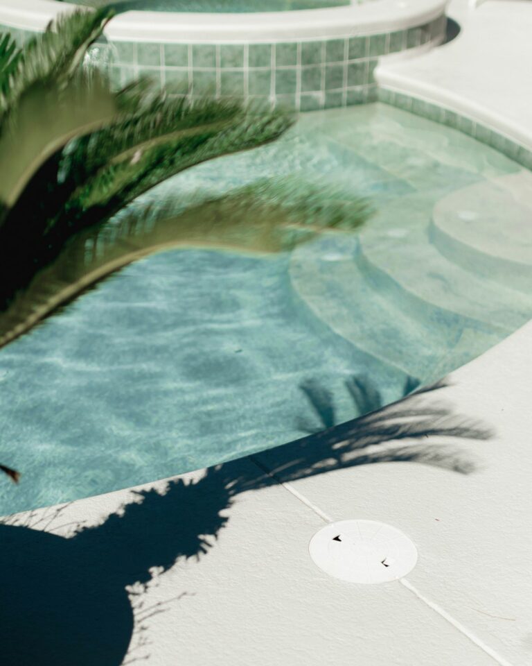 A close-up view of cracked pool tiles and chipped pool coping beside clear blue water.