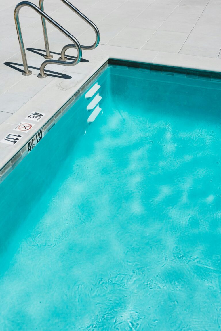 A backyard pool surrounded by updated paver decking and illuminated by modern LED lighting in the evening.
